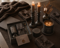 The Ember Gift Box Luxe — heavyweight espresso linen runner, charcoal linen napkins with linen ribbon, matte black pillar candle in solid iron holder, near-black reactive glaze vase with dried botanicals, large-format tobacco and oud candle, wax-sealed palette card