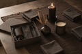The Ember Gift Box Standard — espresso linen runner, charcoal linen napkins, matte black pillar candle, near-black stoneware vase, dried wheat botanical, hand-poured tobacco and oud candle